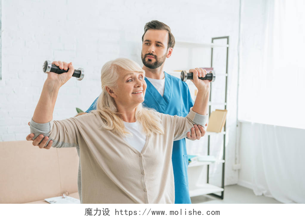 男护士在教奶奶锻炼社会工作者看在微笑的资深妇女训练与哑铃 